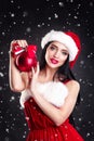 Smiling girl holding a red Christmas tree balls. Women on dress and santa`s hat. Santa`s helper .Attractive happy girl in santa h Royalty Free Stock Photo