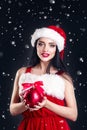 Smiling girl holding a red Christmas tree balls. Women on dress and santa`s hat. Santa`s helper .Attractive happy girl in santa h Royalty Free Stock Photo