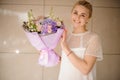 Smiling girl holding a spring bouquet of tender color different flowers with leaves in a purple paper Royalty Free Stock Photo