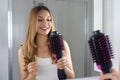 Smiling girl holds round brush hair dryer in her bathroom at home. Young woman looking satisfied her salon one-step brush hair Royalty Free Stock Photo