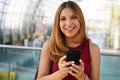 Smiling girl holds smartphone looking at camera in modern train station. Happy confident woman get a refund for her canceled Royalty Free Stock Photo