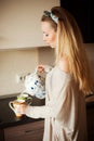 Attractive woman in the kitchen pouring a mug of hot tea from a pot. Having breakfast in the morning Royalty Free Stock Photo