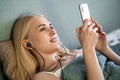 Smiling girl listening music on her smartphone lying on bed in a bedroom Royalty Free Stock Photo