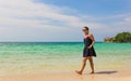 Smiling girl listening to music while walking on beach shore and holding a mobile connected to earphones Royalty Free Stock Photo