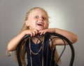 Smiling girl with long hair in dress with beads sitting on chair, on grey