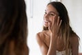 Smiling girl look in mirror do skincare facial routine