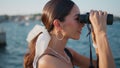 Smiling girl looking binoculars at summer embankment closeup. Happy trendy woman