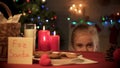 Smiling girl looking from under table at tasty ginger X-mas cookies, having fun Royalty Free Stock Photo