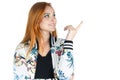 Smiling girl looks and points to the side. Redheaded girl wearing colorful jacket. Summer..