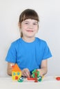 Smiling girl molds toys from plasticine on white table