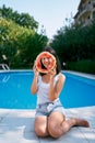 Smiling girl peeking through a hole in a watermelon while sitting by the pool Royalty Free Stock Photo