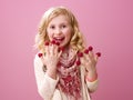 Smiling girl on pink background eating raspberries on fingers