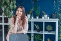 A smiling girl in a pink shirt is looking into the frame. In the background, there is a large number of indoor plants