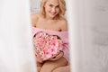 Smiling girl in the pink shirt sitting on the bed holding the heart shape box of rose colored peonies, orchids and roses Royalty Free Stock Photo