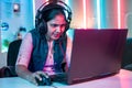 Smiling girl playing live video game on laptop by talking on headphones at home on neon background - concept of vlogger Royalty Free Stock Photo