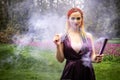 A girl with a smile with bright makeup and colored braids in a purple dress blows artificial purple smoke in a spring Royalty Free Stock Photo