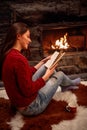 Smiling girl reading book in front of fireplace Royalty Free Stock Photo