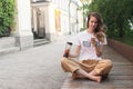 Smiling girl relaxing at street, she is playing music using a smartphone and wearing white headphones