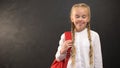 Smiling girl with rucksack smiling on camera on blackboard background, education