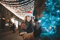 A smiling girl in Santa`s hat stands near a Christmas tree on a New Year`s Eve street decoration, makes a selfie on a smart phon Royalty Free Stock Photo