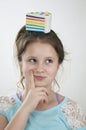 A smiling girl with a sguishy toy cake on her head and forefinger on cheeck Royalty Free Stock Photo