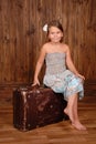 Smiling girl sits on the ancient brown scratched suitcase