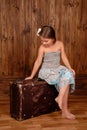 Smiling girl sits on the ancient brown scratched suitcase