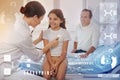 Smiling girl sitting on the bed while a doctor examining her with a stethoscope