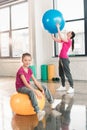 Smiling girl sitting on fitness ball while mother exercising