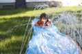 Smiling girl sliding down an outdoor slip and slide. selective focus on water in front of child Royalty Free Stock Photo