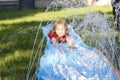 Smiling girl sliding down an outdoor slip and slide. selective focus on water in front of child Royalty Free Stock Photo