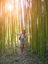 Smiling girl standing in bamboo grove holding tree trunks on warm spring day Royalty Free Stock Photo