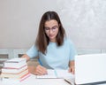 A smiling girl student sitting at a table with a laptop writes a task in a notebook. Girl student studies at home. Royalty Free Stock Photo