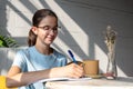 Smiling girl student writes homework with a pen in a notebook in a cafe. Back to school concept. Royalty Free Stock Photo