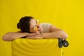 Smiling girl in sunglasses laid her head on a suitcase on a yellow background. Happy woman with hand bag awaiting trip Royalty Free Stock Photo