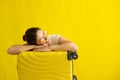 Smiling girl in sunglasses laid her head on a suitcase on a yellow background. Happy woman with hand bag awaiting trip Royalty Free Stock Photo