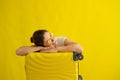 Smiling girl in sunglasses laid her head on a suitcase on a yellow background. Happy woman with hand bag awaiting trip Royalty Free Stock Photo