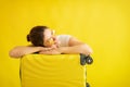 Smiling girl in sunglasses laid her head on a suitcase on a yellow background. Happy woman with hand bag awaiting trip Royalty Free Stock Photo