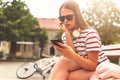 Smiling young woman sitting on a bench in the summer using smart phone Royalty Free Stock Photo