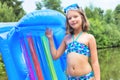 Shot of smiling girl in swimwear standing with pool raft at lakeshore