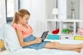 Smiling girl with tablet pc sitting on bed at home