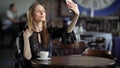 Smiling girl taking selfie. Young smiling female inelegant dress sitting at table in cafe and taking selfie.