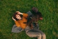 Smiling girl in vintage clothes and hat playing with dog on lawn, top view. Cheerful owner relaxing with her pet on the lawn in