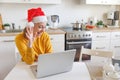 Smiling girl wearing Santa hat waving hand video calling family by webcam. Woman with laptop having virtual meeting chat Royalty Free Stock Photo