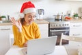 Smiling girl wearing Santa hat waving hand video calling family by webcam. Woman with laptop having virtual meeting chat Royalty Free Stock Photo