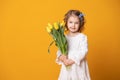 Smiling girl in white dress on yellow background. Cheerful happy child with tulips flower bouquet Royalty Free Stock Photo