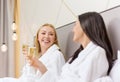 Smiling girlfriends with champagne glasses in bed