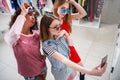 Smiling girlfriends wearing stylish sunglasses having fun time taking selfie with mobile phone while doing shopping in