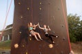 Smiling girls giving high five hanging on ropes at artificial climbing training wall and insured by friends on belaying