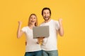 Smiling glad millennial caucasian guy and lady in white t-shirts hold laptop, making victory sign with hands Royalty Free Stock Photo